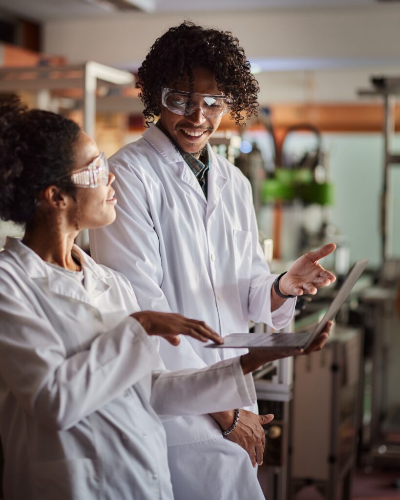 Happy African American students of science talking while working on a computer in robotics laboratory.